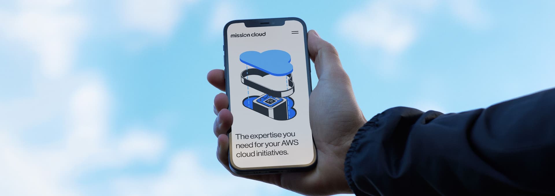 Hand holding a smartphone displaying a website with a cloud-themed graphic and text that reads, "The expertise you need for your AWS cloud initiatives," against a blue sky background.
