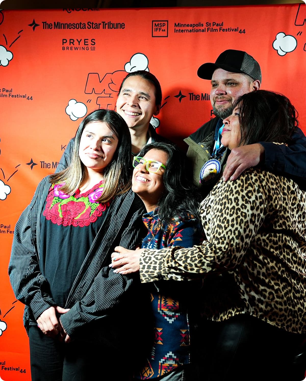 Group of five people smiling and posing together in front of an orange backdrop with logos for The Minnesota Star Tribune, Pryes Brewing Co, and the Minneapolis St Paul International Film Festival.