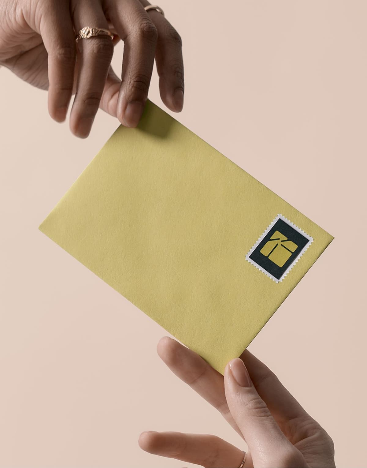 Two hands exchanging a yellow envelope with a black and gold gift box stamp on a beige background.