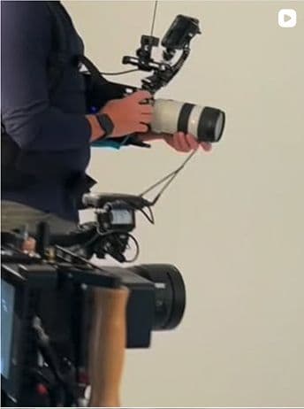 Person wearing a harness rig holding a professional camera with a large telephoto lens, with another camera visible in the foreground.
