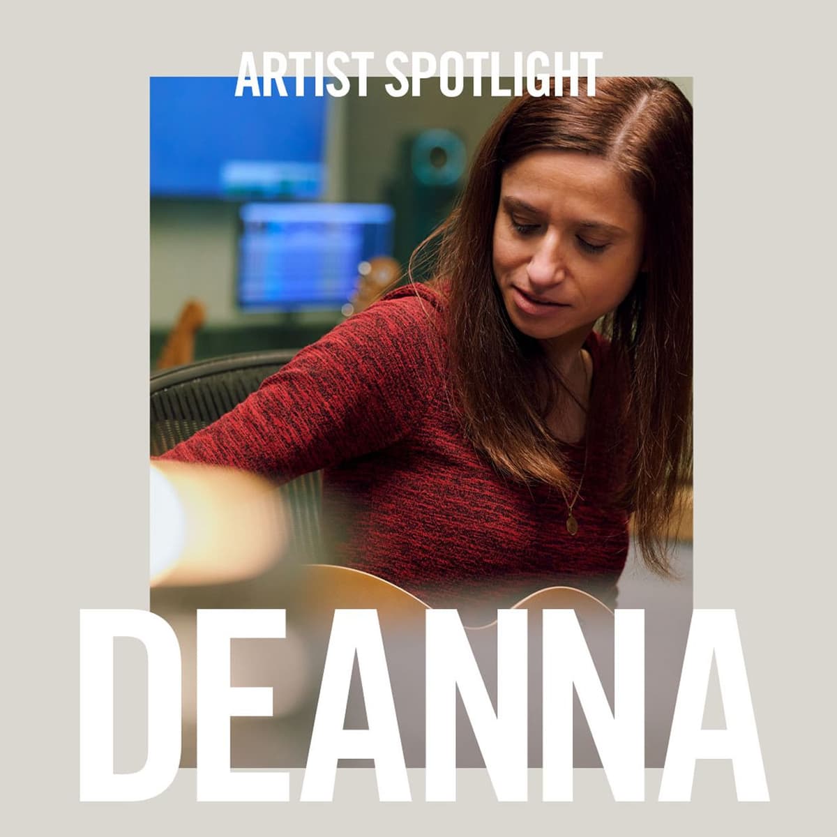 Photo of a woman with long brown hair wearing a red sweater, looking down while playing a guitar, with a blurred music studio background. Text above reads "Artist Spotlight" and large text below reads "Deanna."