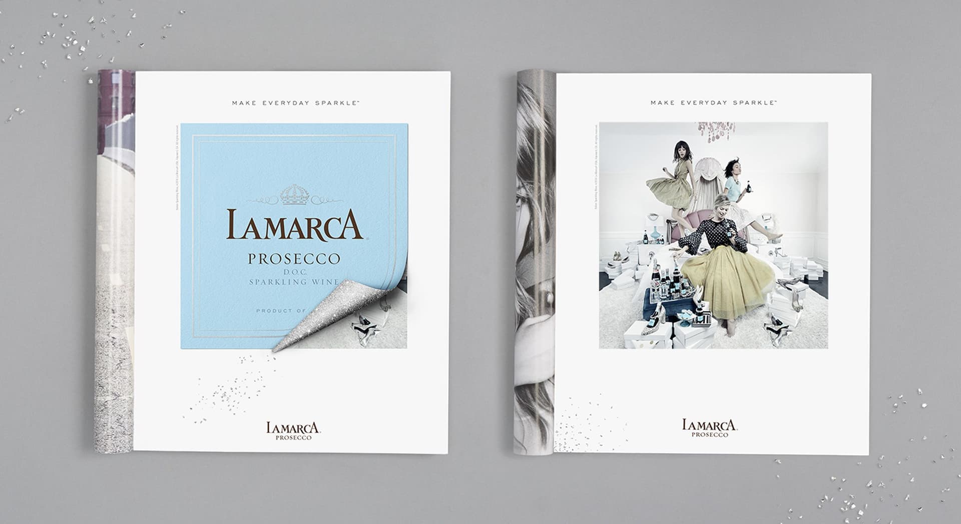 Two LaMarca Prosecco brochures on a gray surface, one showing a folded-back blue label design with the text "LaMarca Prosecco," the other depicting three women in vintage-style dresses surrounded by gift boxes and sparkling wine bottles, both with the tagline "Make Everyday Sparkle."