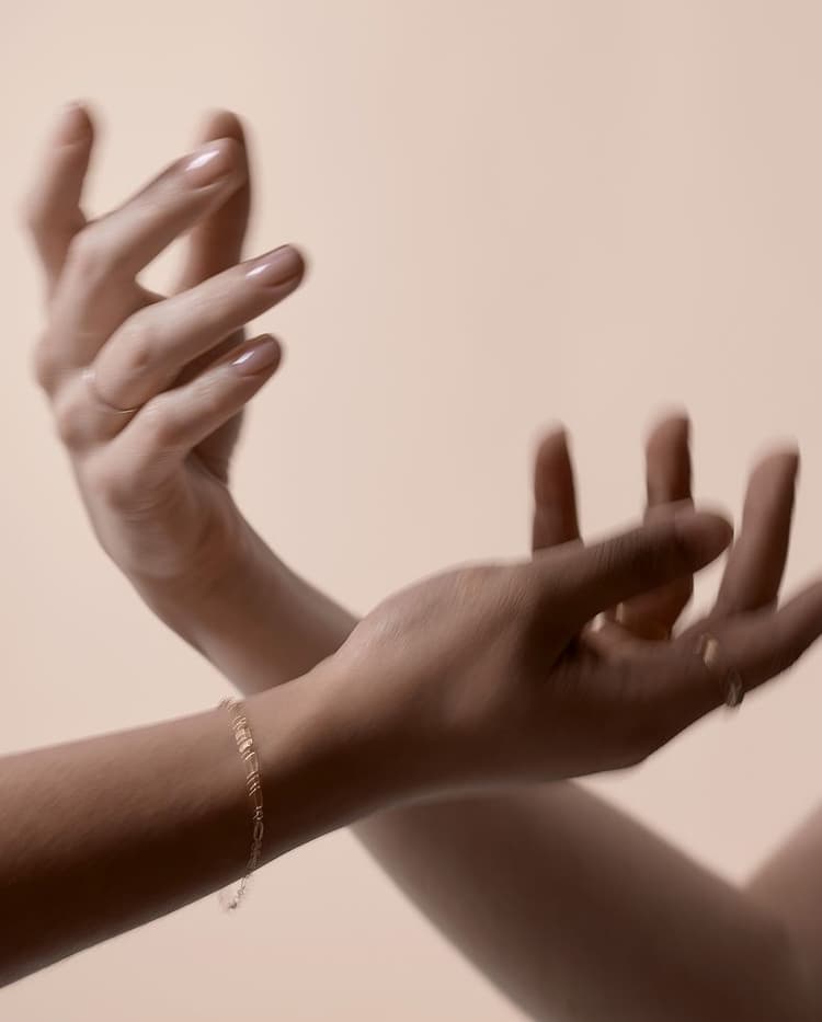 Blurred close-up of two hands with interlaced fingers against a neutral background, one wearing a bracelet and a ring.