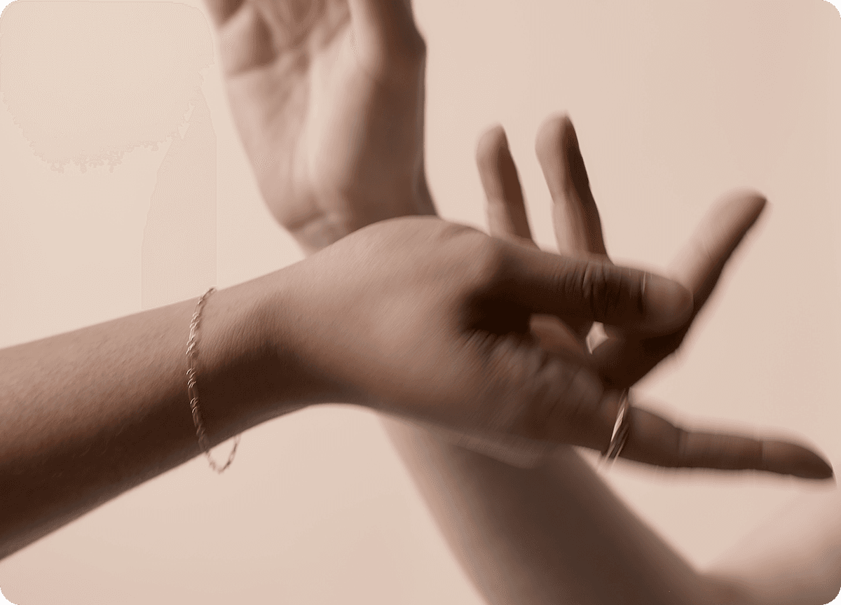 Two hands crossing over before a solid tan background. The hands are slightly blurred.