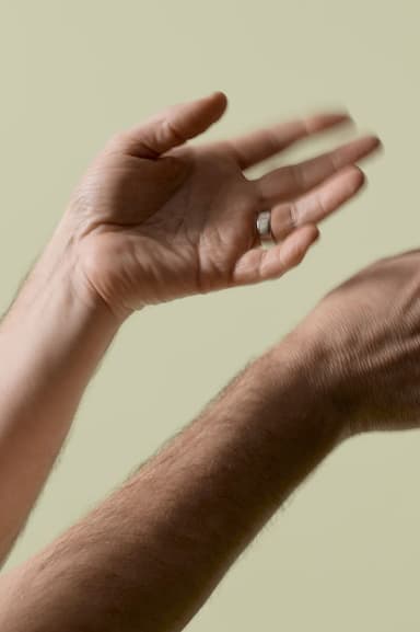 Close-up image of two hands, one wearing a ring, in motion against a plain beige background.
